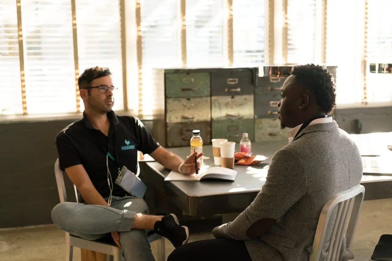 Life Coach Wearing Black Polo Shirt and Gray Pants Sitting on White Chair