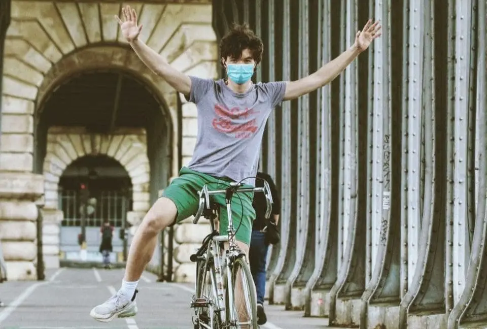 Young man riding bike with outstretched arms wearing a face mask