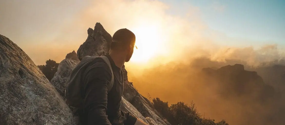 Man on top of a mountain looking at the sunset