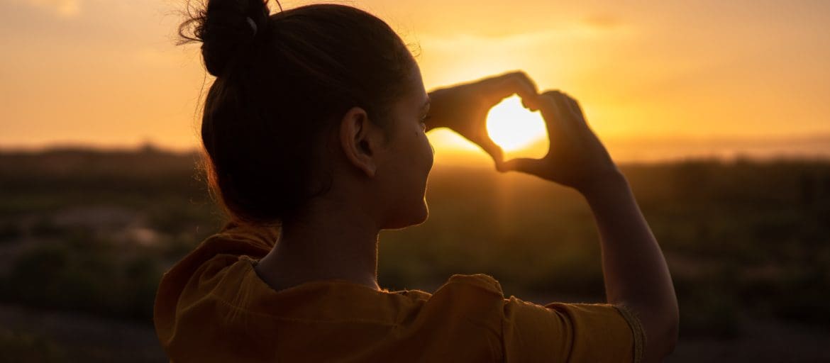 Woman drawing a sunset with her hands against the sunset